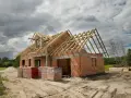 Budowa domu 100m2 w toku. Ściany z cegły, drewniany szkielet dachu, materiały budowlane na placu.