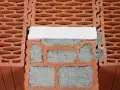 Zbliżenie na pustaki ceramiczne z widocznymi pustymi przestrzeniami i zaprawą. Pokazane są wymiary pustaka i sposób ich układania.