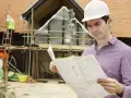 Kierownik budowy w kasku analizuje plany. Jego zakres obowiązków obejmuje nadzór nad postępem prac budowlanych.