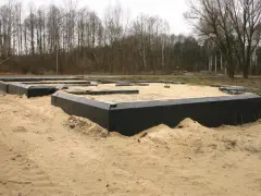 Nowoczesna izolacja fundamentów bez odkopywania. Czarna folia zabezpiecza piaskowe podłoże budowy.
