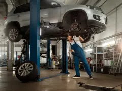 Mechanik pracuje pod samochodem na podnośniku. Szacowany koszt budowy warsztatu 100m2.