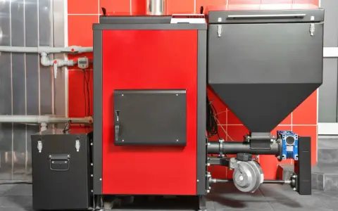 Nowoczesny piec na pellet, idealny jako jaki piec na pellet do domu 120m2. Czerwono-czarna obudowa, zasobnik na pellet i elementy instalacji.