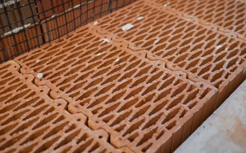Rzędy pustaków ceramicznych, każdy o wymiarach pustak max, czekają na budowę. Siatka zbrojeniowa w tle.