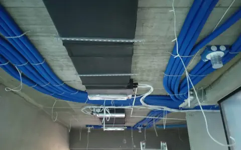 Instalacja rekuperacji w bloku: niebieskie rury wentylacyjne i czarny kanał wentylacyjny zamontowane na suficie.