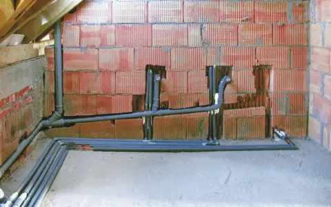 Instalacja hydrauliczna w trakcie budowy. Widoczne rury odprowadzające, pion sanitarny z odpowietrzeniem zgodnym z normą.