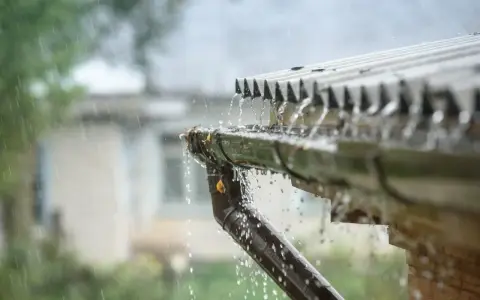 Intensywny deszcz spływa rynną, a w tle widać dom. Kiedy wejdzie w życie podatek od deszczu?