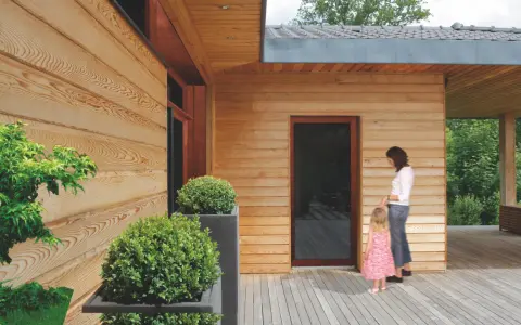 Piękna elewacja z drewna, której impregnacja zapewnia trwałość i naturalny wygląd. Kobieta z dzieckiem na tarasie.