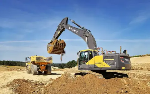 Koparka Volvo wysypuje ziemię do wywrotki. Prace ziemne, ułożenie rur w wykopie cennik bez materiału.