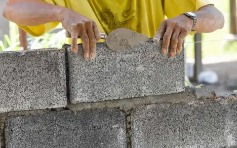 Budowniczy układa bloczek betonowy, zastanawiając się, ile waży bloczek betonowy.