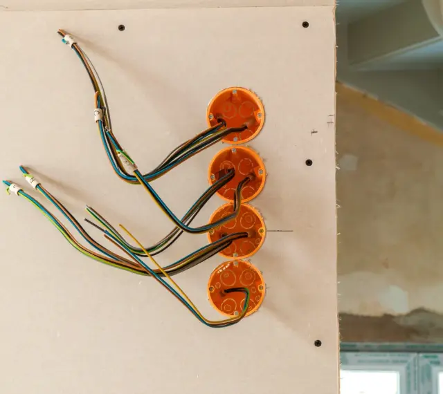 Instalacja elektryka w domu: pomarańczowe puszki i kolorowe przewody przygotowane do montażu gniazdek i włączników.