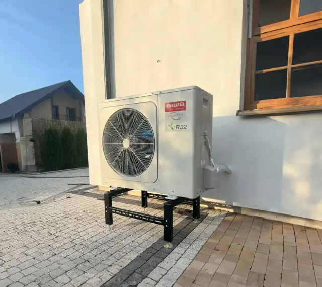 Pompa ciepła Aiwa Inverter R32 na stelażu przed budynkiem. Zastanawiasz się, jaką pompę ciepła wybrać?